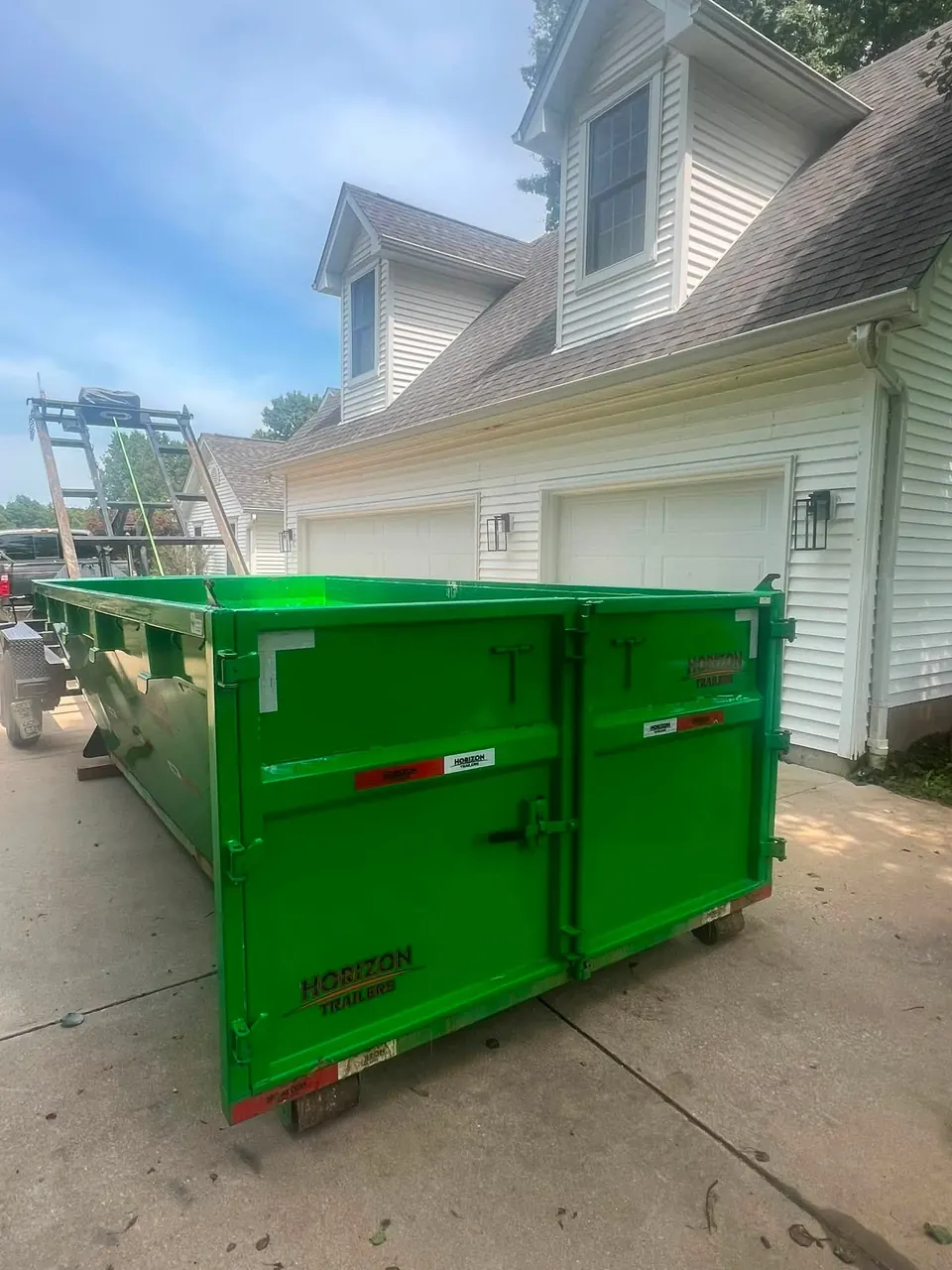 Green TX2 14-yard roll-off dumpster placed on a driveway in front of a white two-car garage